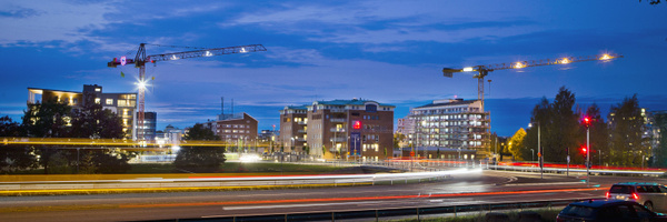 Vy över centrala Karlstad i skymning med byggkranar, moderna flerbostadshus och ljusspår från trafik som visar rörelse i staden.